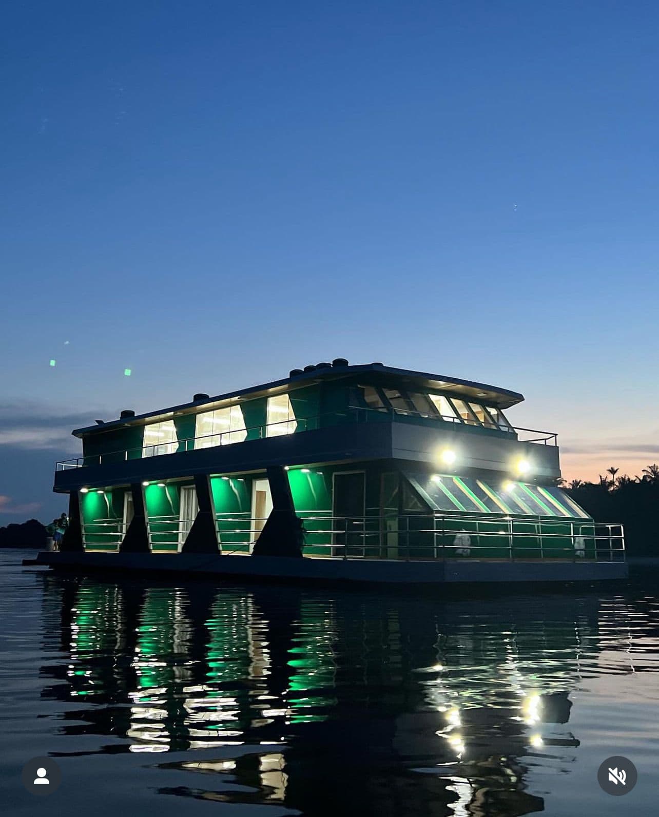 Barco-hotel Barcelos Eco Fishing ancorado no Rio Negro ao crepúsculo com iluminação verde refletida na água