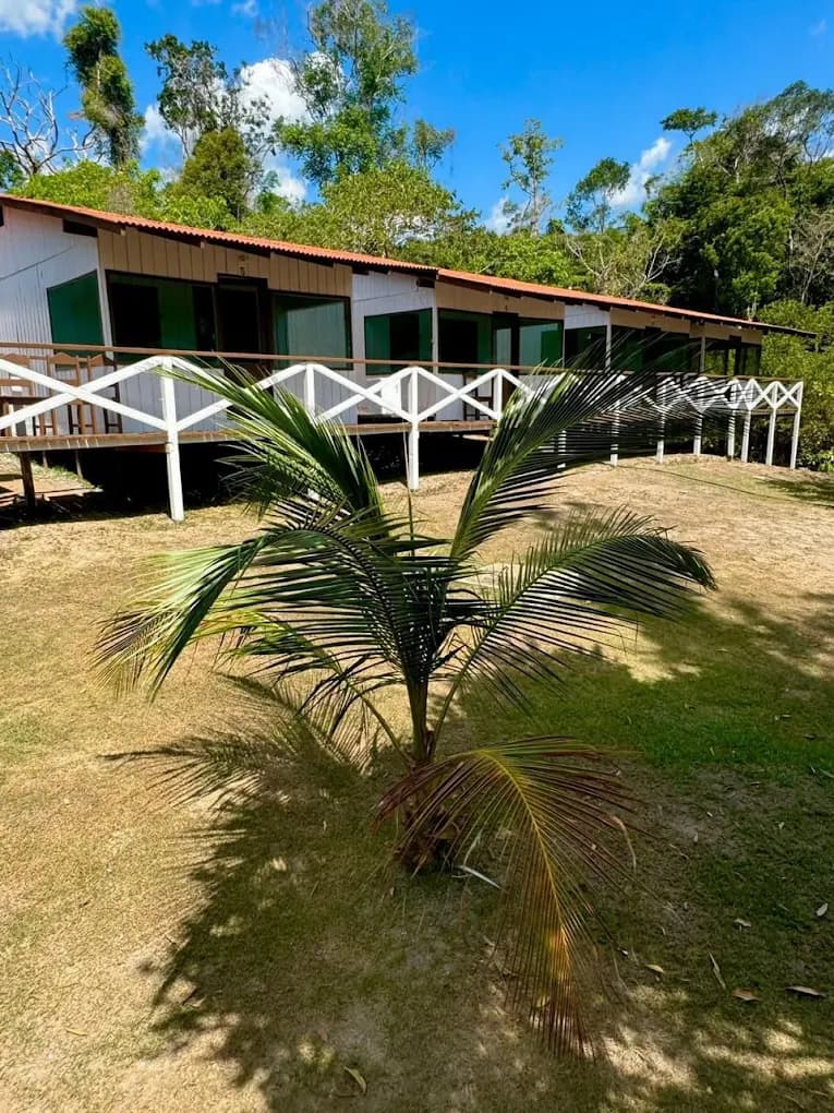 Fachada principal da Pousada Acari com varanda frontal, telhado vermelho e jardim no meio da Amazônia