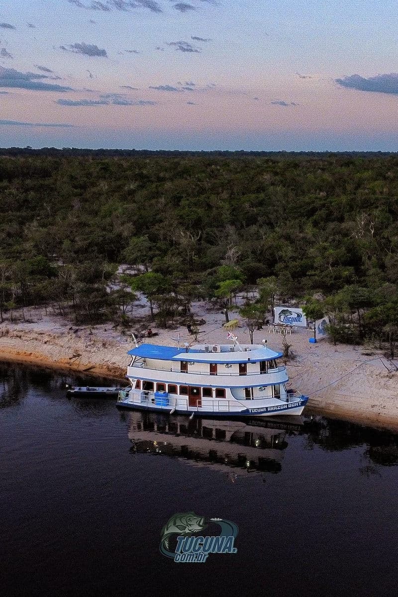 Vista aérea do Tucuna Amazon Boat ancorado em praia de areia branca do Rio Negro ao entardecer.